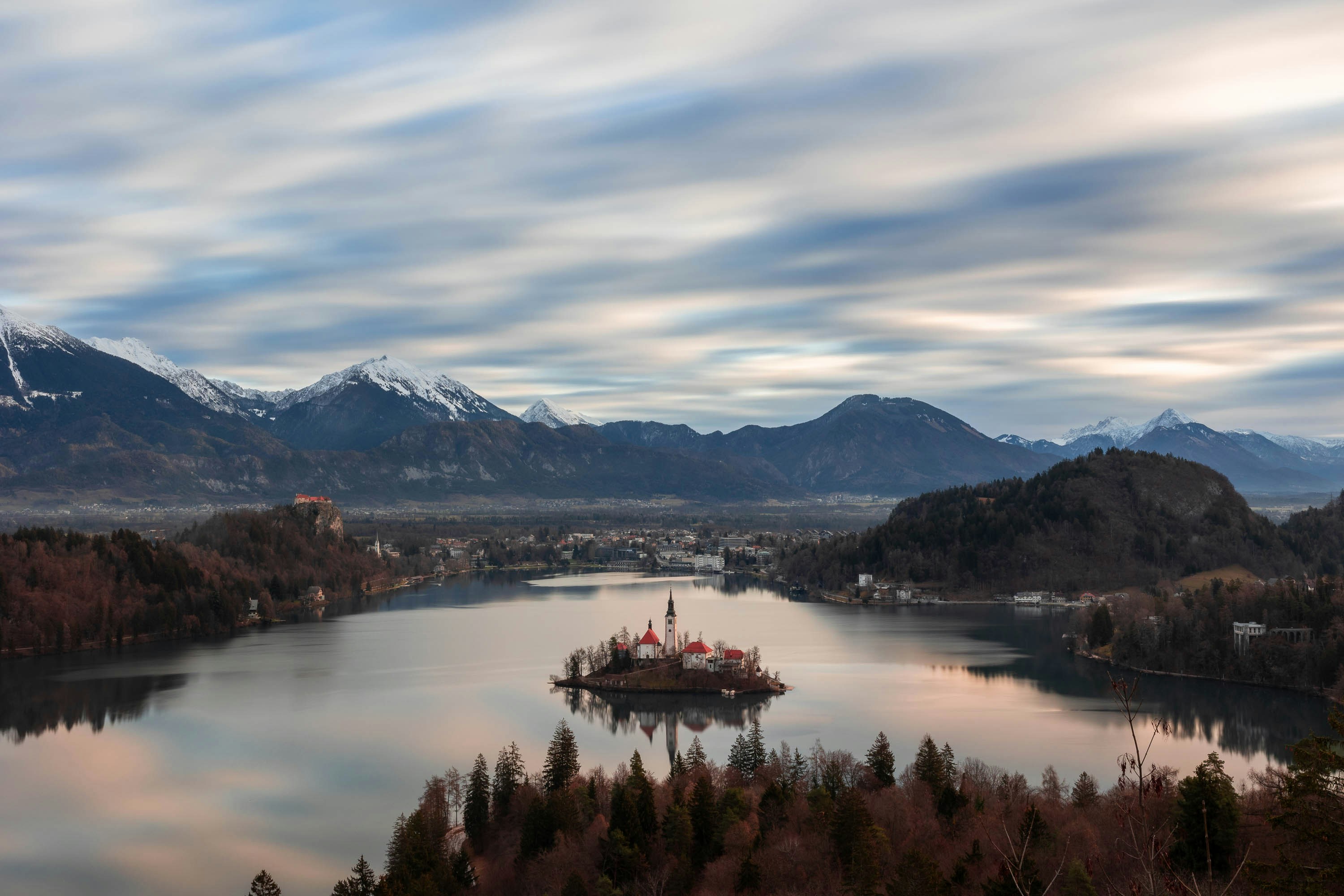 a lake surrounded by trees and mountains under a cloudy sky, Bled lake with the famous island with the church in Slovenia