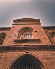 An upward view of a historic brick building with arched windows and detailed masonry. The architecture is characterized by intricate brickwork and an imposing facade that suggests an older architectural style.