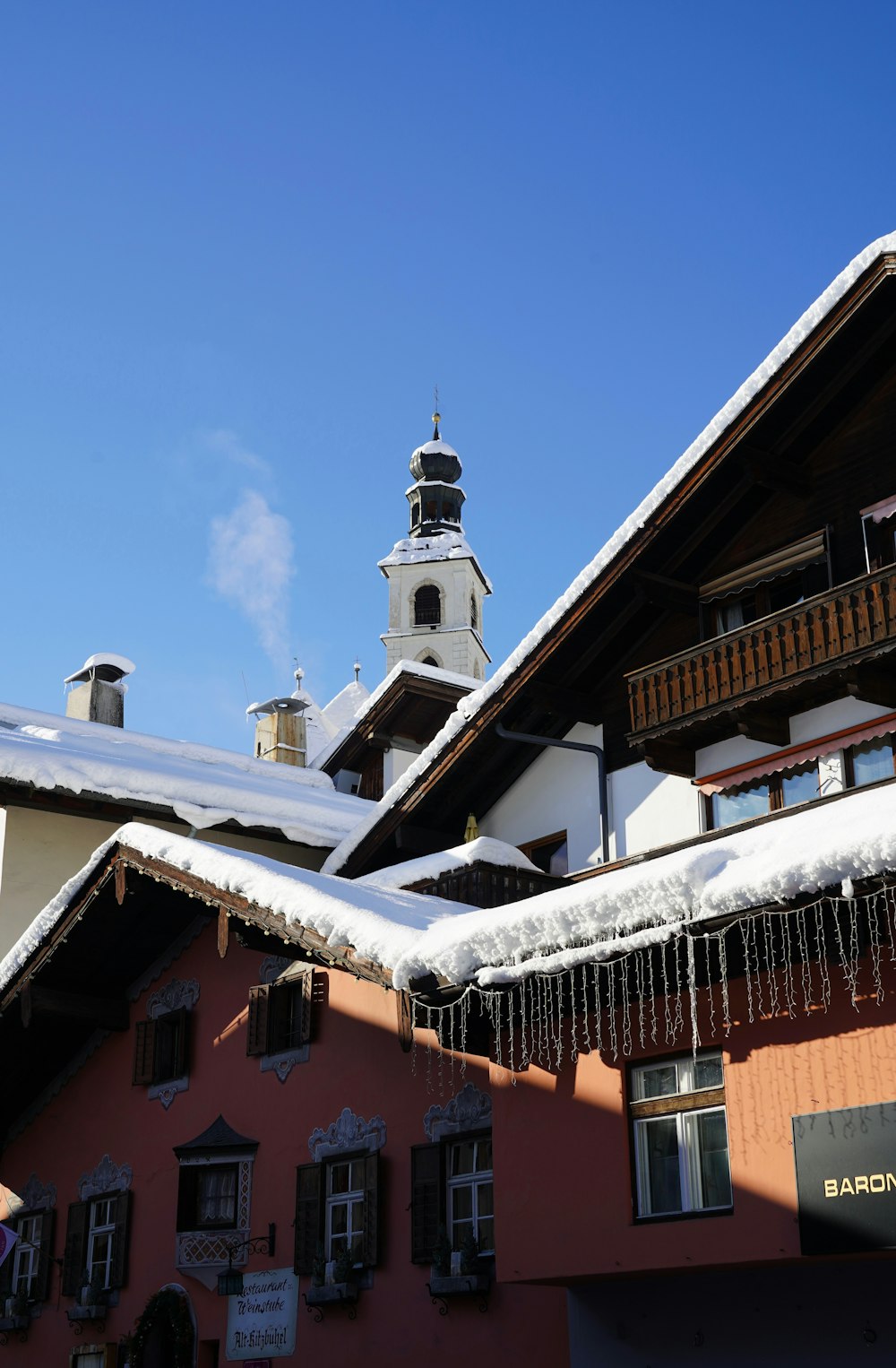 um edifício com neve no telhado e uma torre do relógio ao fundo