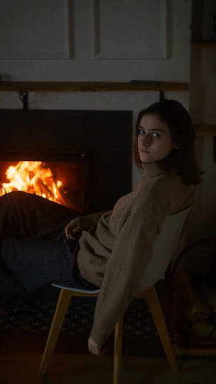 Cozy black and gray sweater draped over a wooden chair beside a crackling fireplace.
