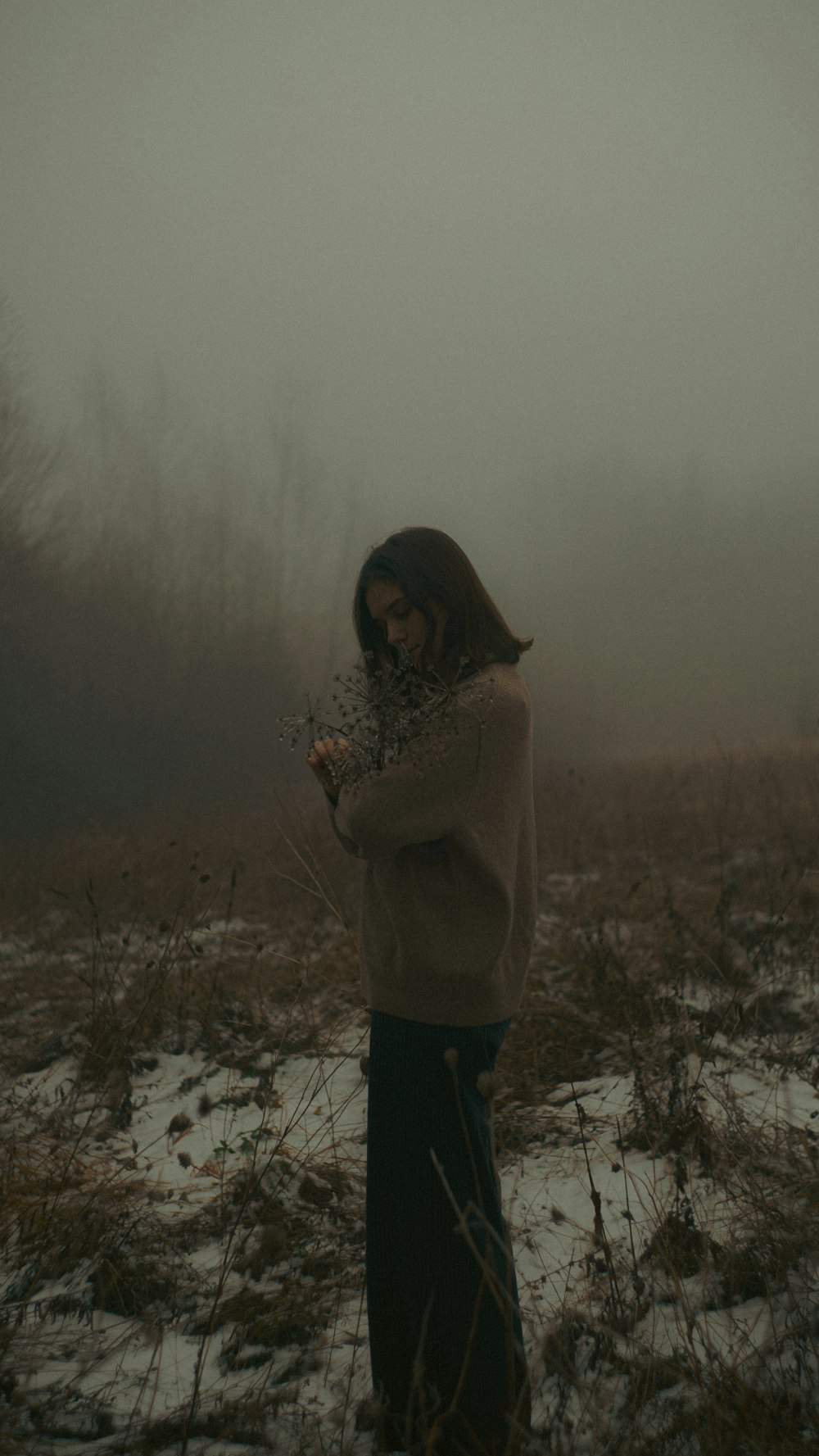 a woman standing in a snowy field holding a plant