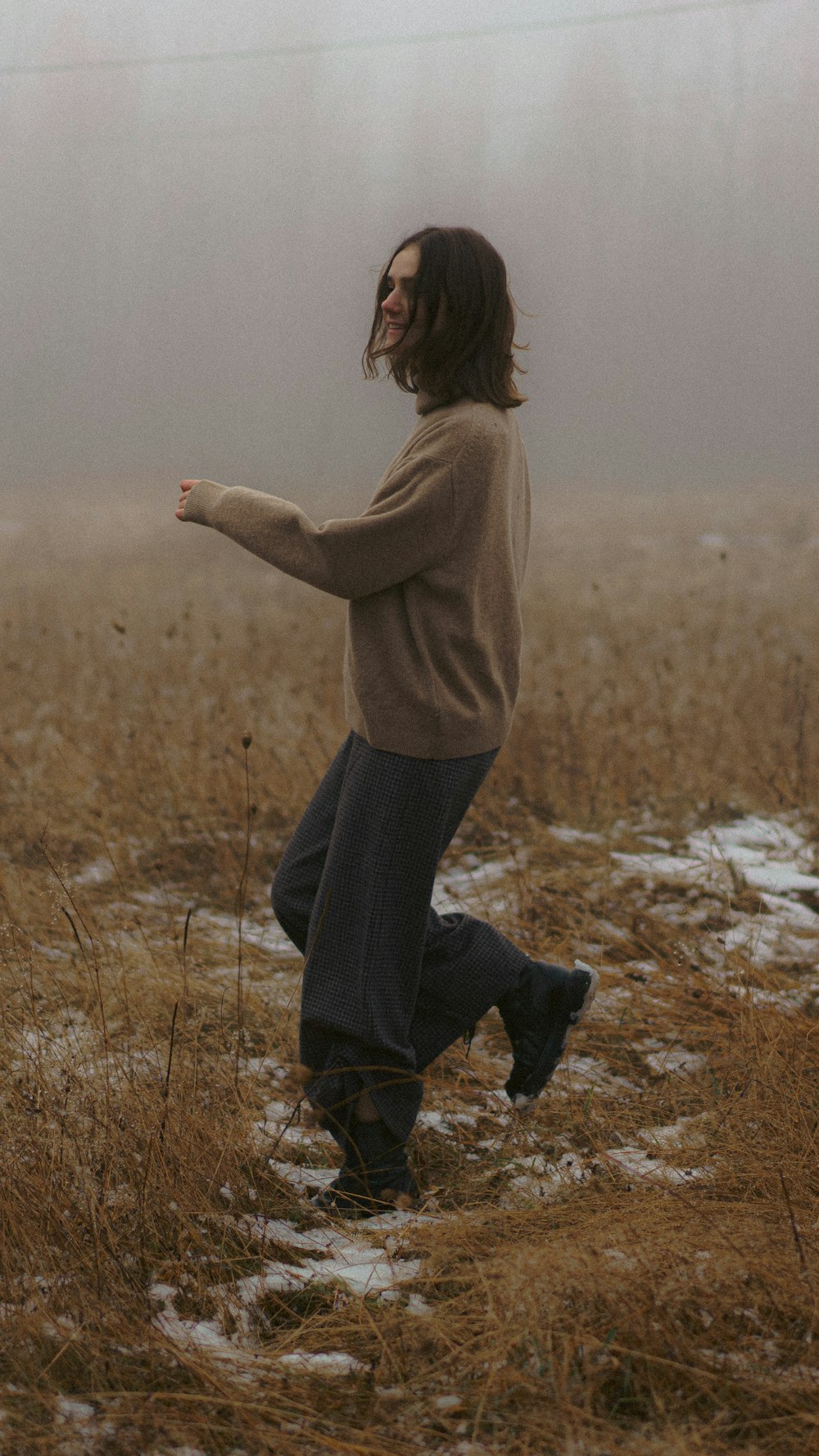 a woman walking through a field on a foggy day