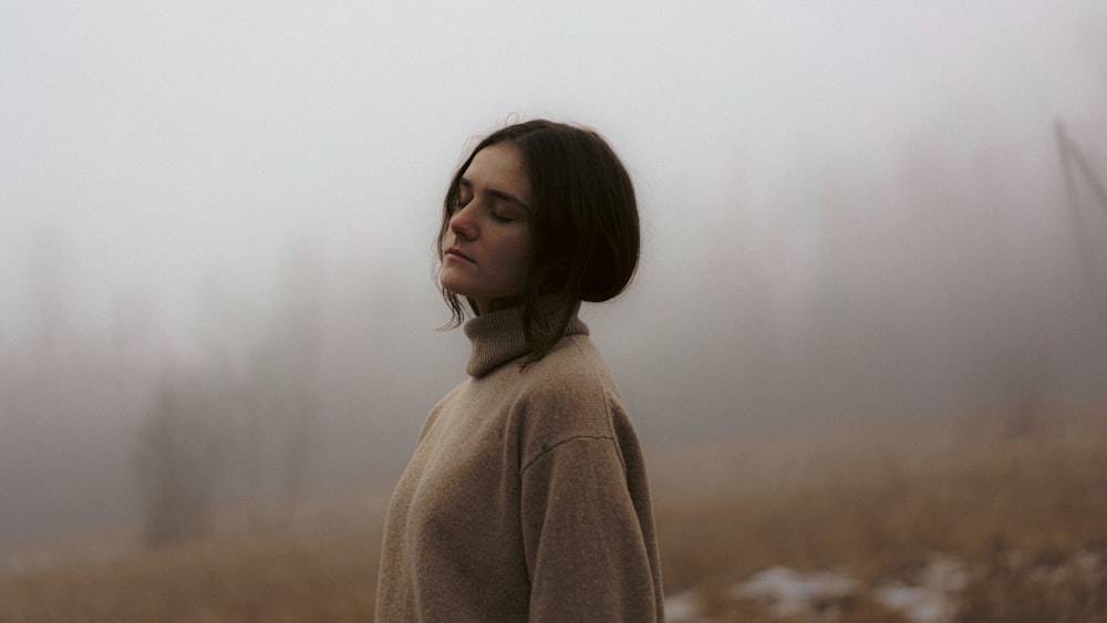 a woman standing in a foggy field with her eyes closed