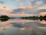 A serene landscape photo featuring a calm lake reflecting a colorful sunset sky.