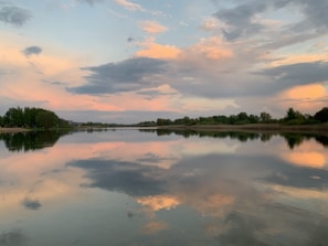 A serene landscape photo featuring a calm lake reflecting a colorful sunset sky.