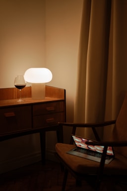 A cozy wooden desk with a vintage whiskey bottle, a notebook, and a pen beside a softly glowing lamp.