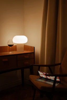 Cozy workspace with a laptop and a personalized wine bottle on a wooden table under warm lighting.