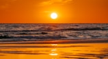 the sun is setting over the ocean on the beach