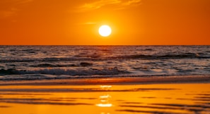 the sun is setting over the ocean on the beach
