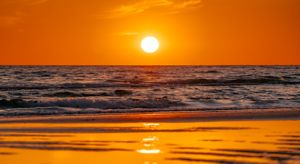 the sun is setting over the ocean on the beach