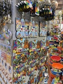A display of colorful souvenirs featuring the word 'Barcelona' in various designs, alongside vibrant ceramic items. The image showcases keychains, magnets, and decorative pieces with artistic representations of landmarks. Rows of brightly painted bowls and dishes add to the vibrant atmosphere.