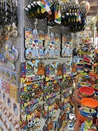 A display of colorful souvenirs featuring the word 'Barcelona' in various designs, alongside vibrant ceramic items. The image showcases keychains, magnets, and decorative pieces with artistic representations of landmarks. Rows of brightly painted bowls and dishes add to the vibrant atmosphere.