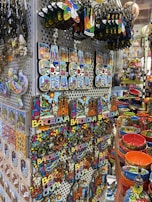 A display of colorful souvenirs featuring the word 'Barcelona' in various designs, alongside vibrant ceramic items. The image showcases keychains, magnets, and decorative pieces with artistic representations of landmarks. Rows of brightly painted bowls and dishes add to the vibrant atmosphere.