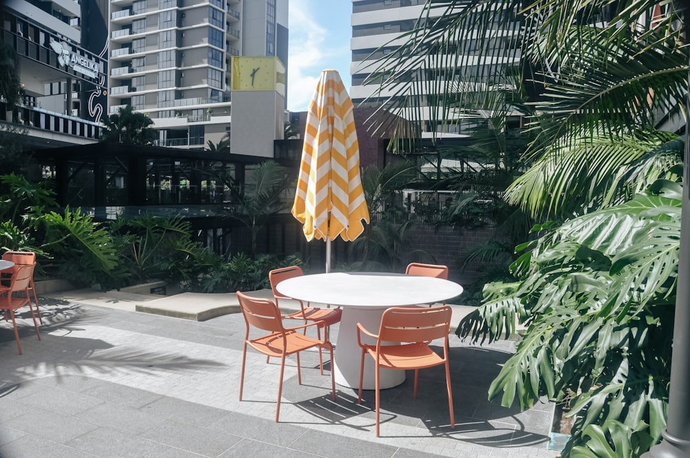 a white table with orange chairs and an umbrella