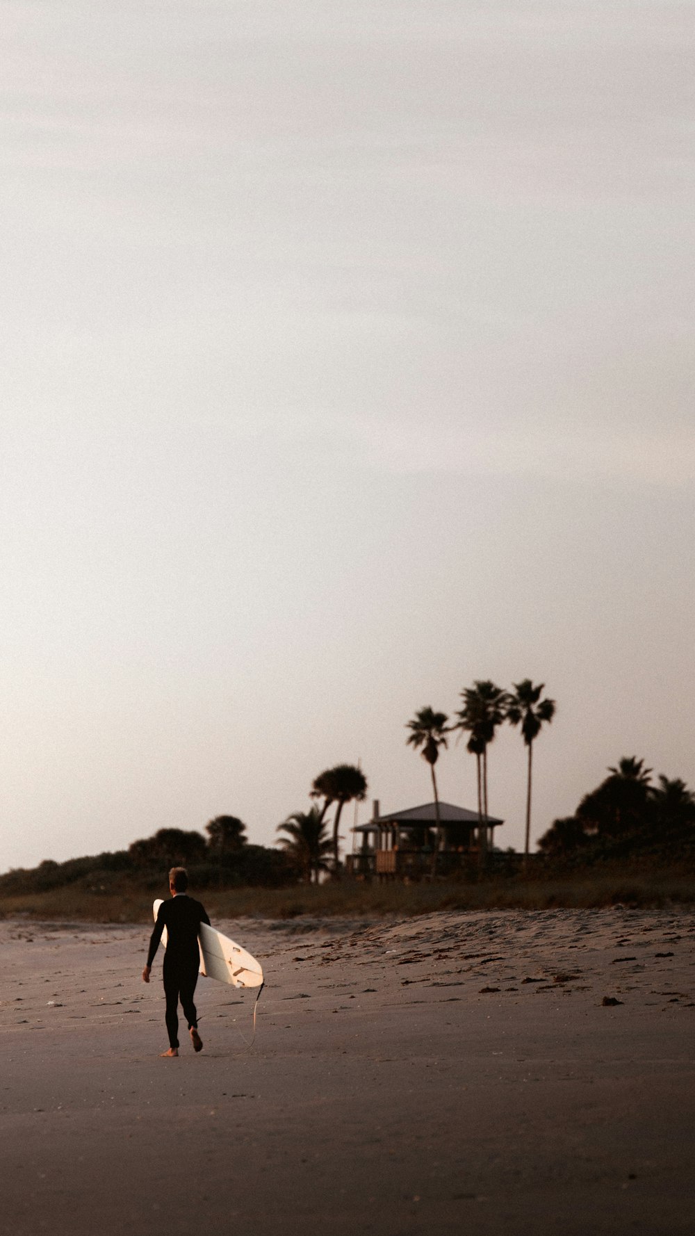 a man walking across a beach holding a surfboard