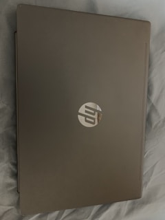 A closed laptop with a metallic finish, displaying a logo on the top. The laptop is placed on a soft, light-colored fabric surface.