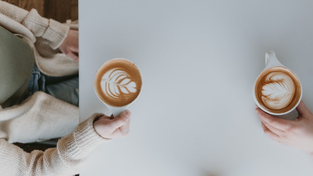 a person holding two cups of coffee in their hands