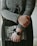 A person is holding a book titled 'New and Selected Poems' while wearing a dark-colored watch. The person is dressed in a grey textured sweater and a dark skirt with subtle patterns. The framing suggests a calm and introspective moment.