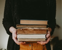 A smiling person holding a stack of well-loved books at a local book fair.