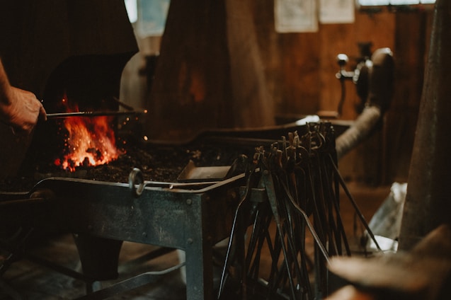 A craftsman working at his forge with supportive hands helping him.