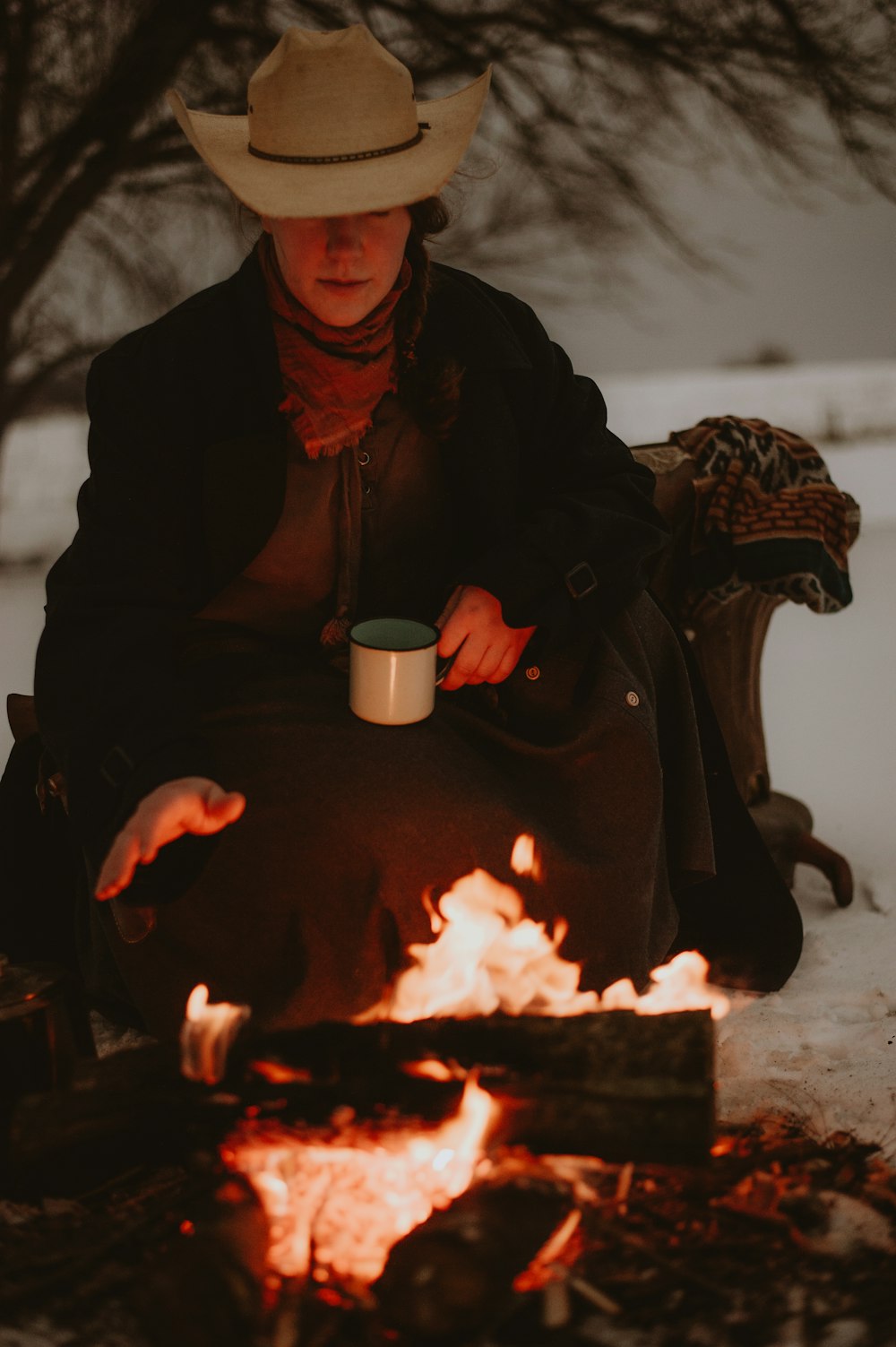 a woman sitting in front of a fire with a cup of coffee