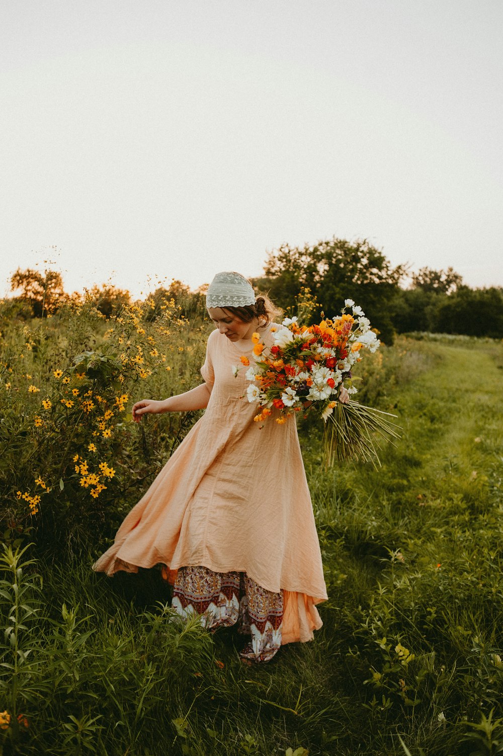 a woman walking through a field holding a bouquet of flowers