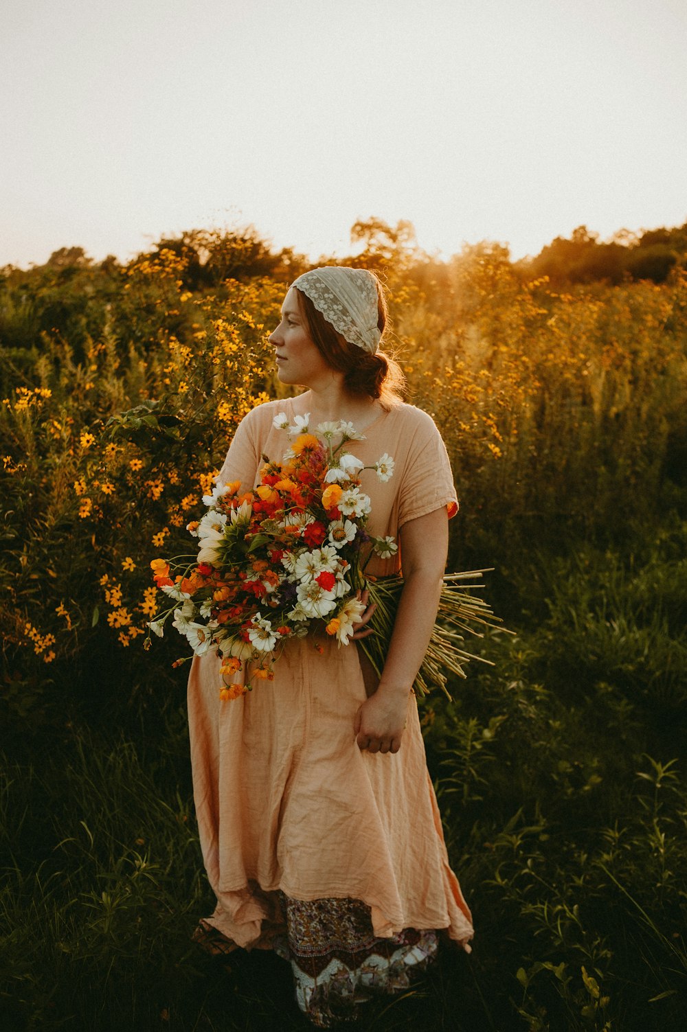 a woman standing in a field holding a bouquet of flowers