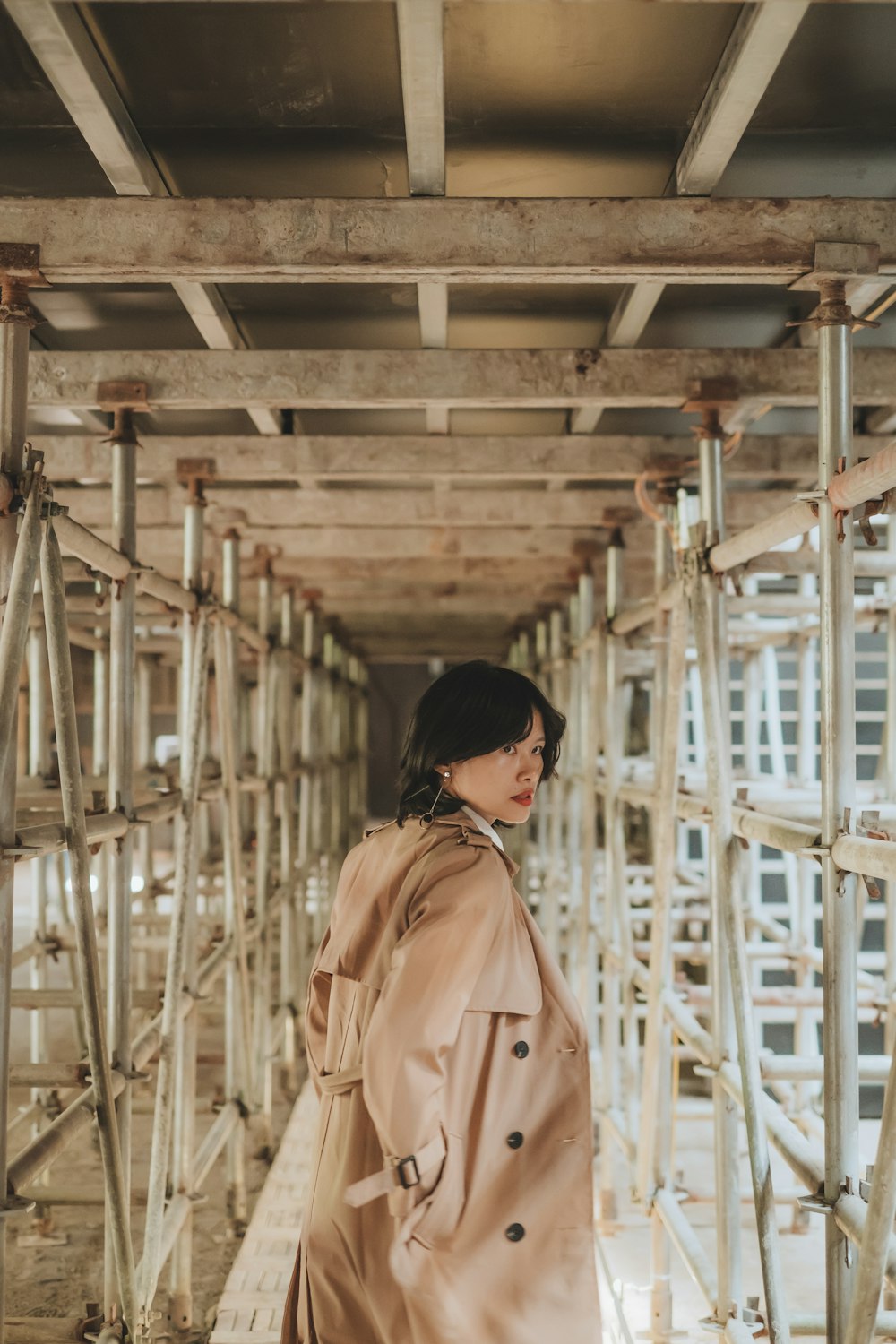 a woman in a trench coat standing on a bridge