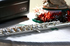 A close-up view of a silver flute placed on a textured surface beside a dark box and festive decorations.