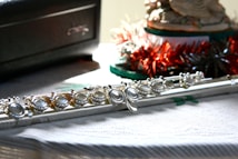 A close-up view of a silver flute placed on a textured surface beside a dark box and festive decorations.