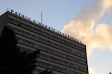 A multi-story building with a message in Spanish on its rooftop, set against a sky with clouds. The building has numerous windows and appears to have air conditioning units attached to some of them.