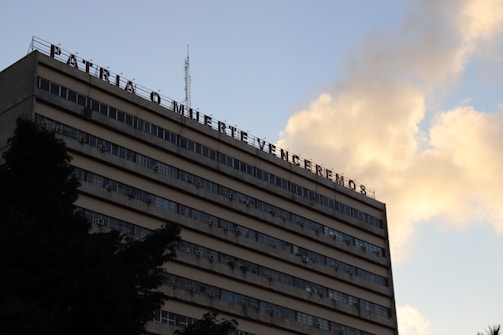 A multi-story building with a message in Spanish on its rooftop, set against a sky with clouds. The building has numerous windows and appears to have air conditioning units attached to some of them.