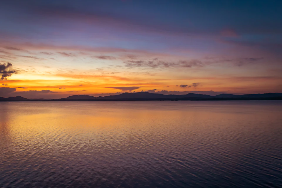 Serene sunset over calm waters with vibrant orange and blue hues behind mountains