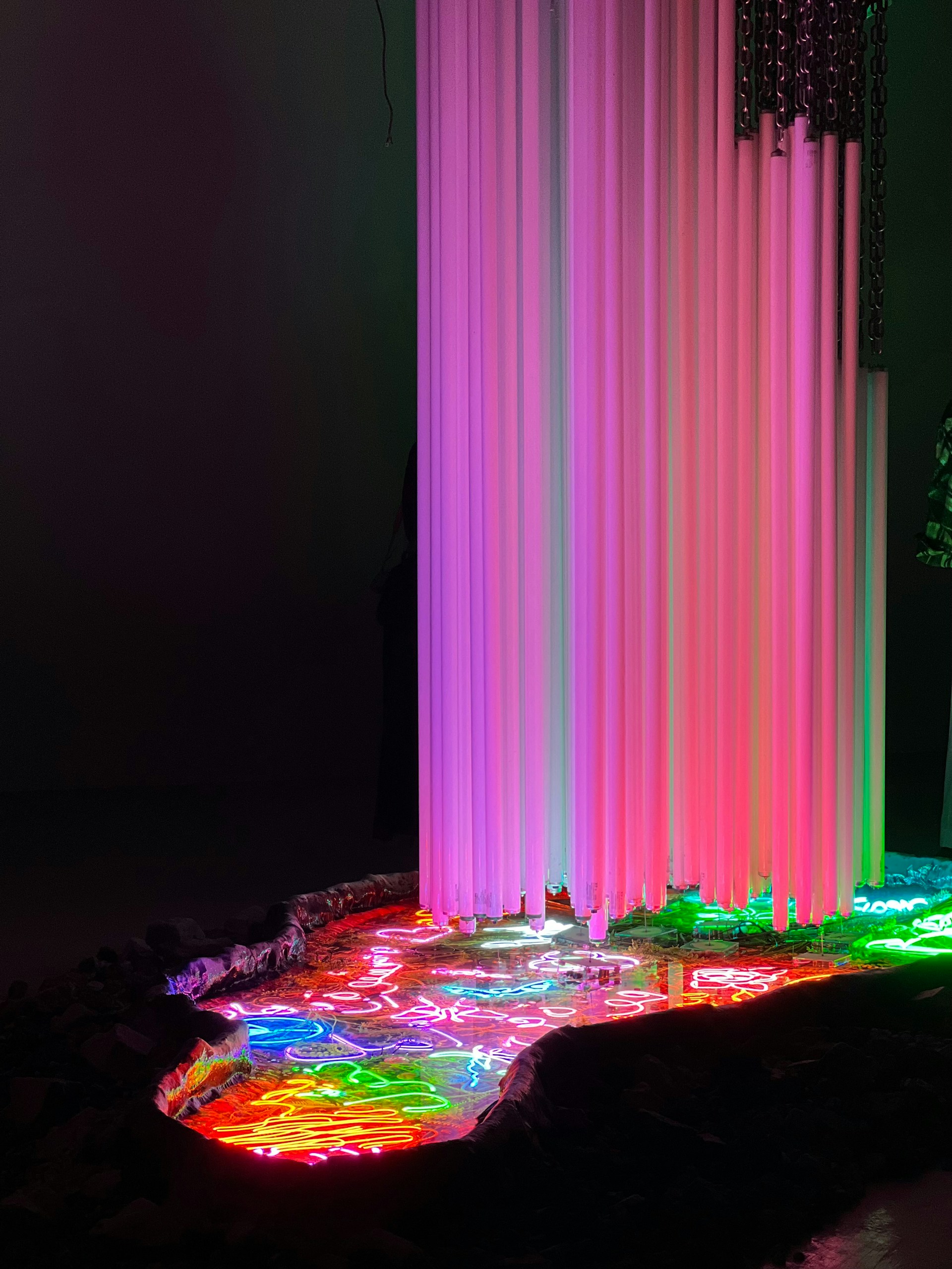 A vibrant light installation glowing with shifting hues of blue, purple, and pink, casting futuristic patterns on a sleek urban wall.