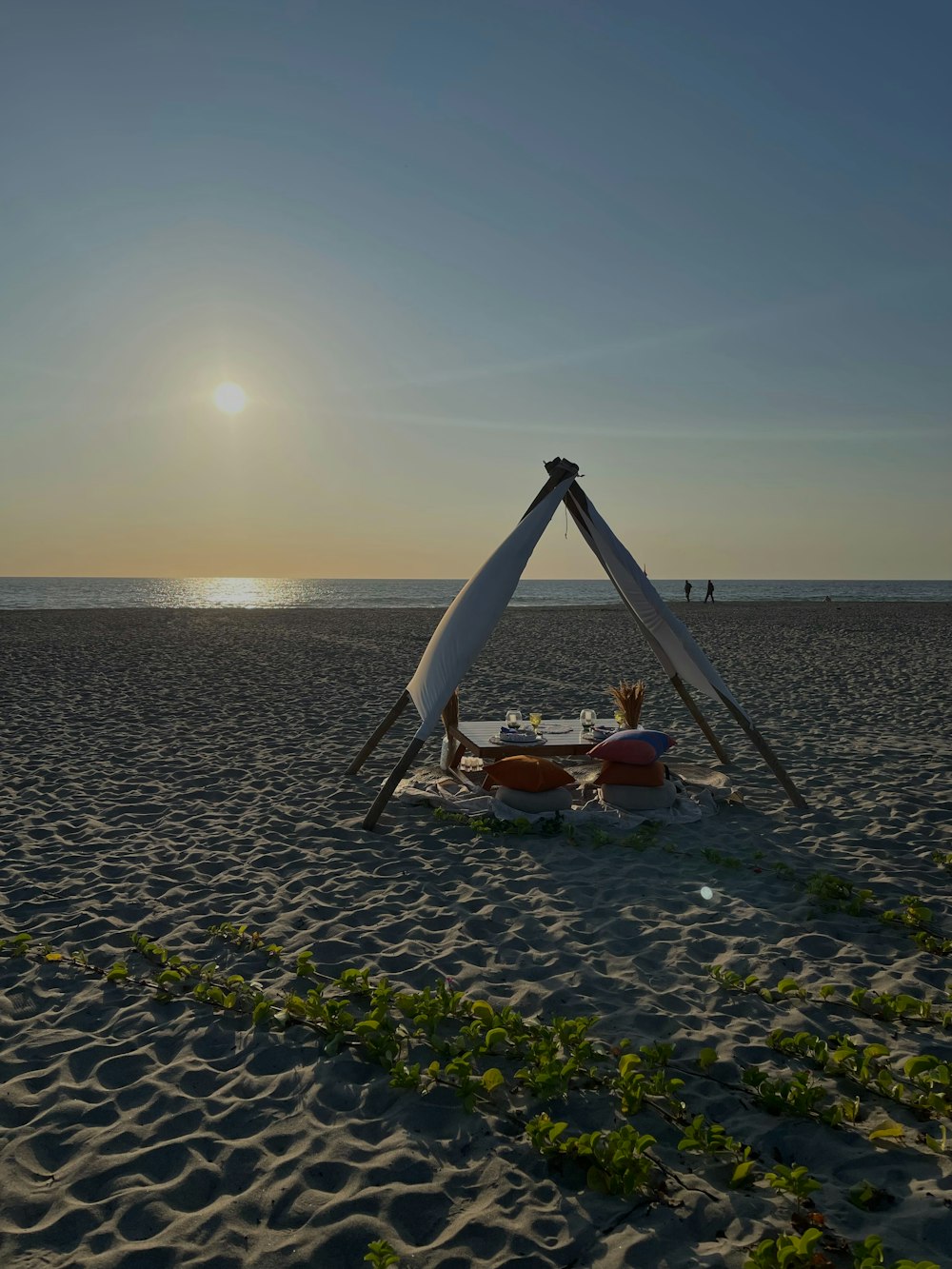 a tent set up on the beach with people sitting around it