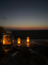 A serene beach scene at sunset with cozy seating and softly lit tables by the sea.