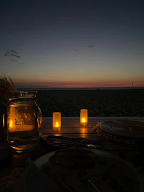 A serene beach scene at sunset with cozy seating and softly lit tables by the sea.