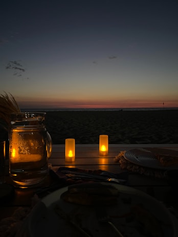 A honeymoon couple enjoying a candlelit dinner on a private beach with soft golden lighting.