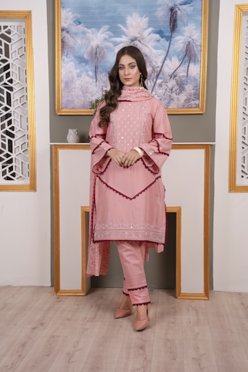 Elegant woman in a blush pink embroidered kurta standing gracefully in a softly lit room.