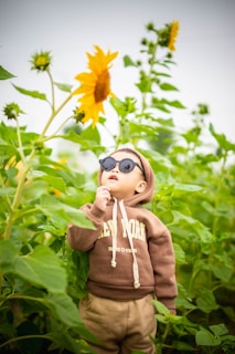 a young boy wearing sunglasses standing in a field of sunflowers