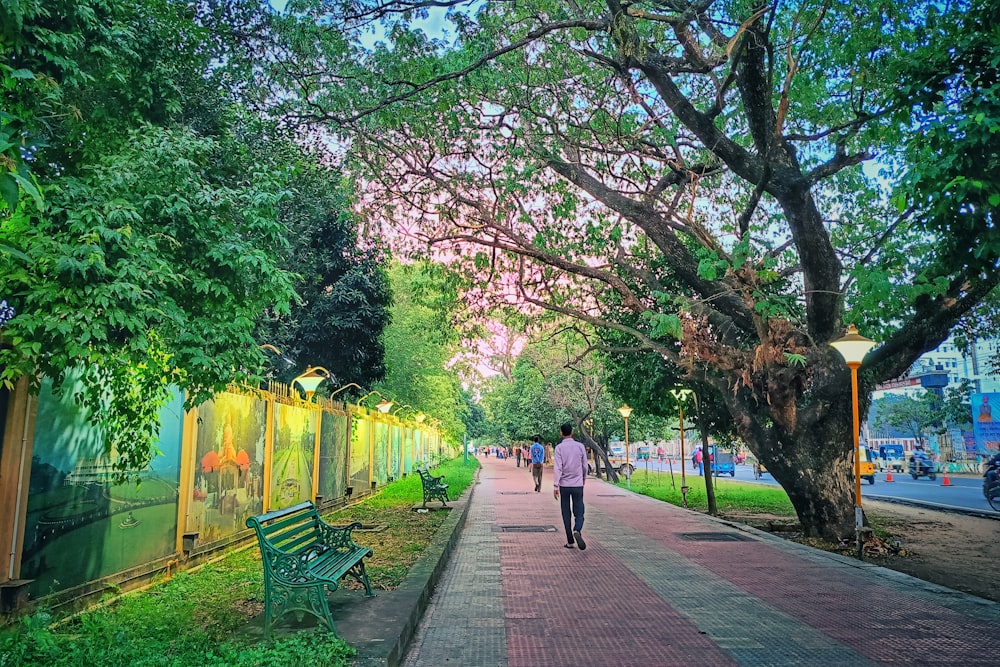 a woman walking down a sidewalk next to a green park bench