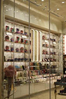 A brightly lit retail store display showcasing a variety of colorful packaged products. The shelves are filled with items like chocolates, candies, and gift boxes. Large glass windows allow a view of the interior, which is organized with sections labeled 'Bestsellers' and 'Heritage'. Decorative elements such as an oversized pink ice cream cone and elegant wallpaper enhance the visual appeal.