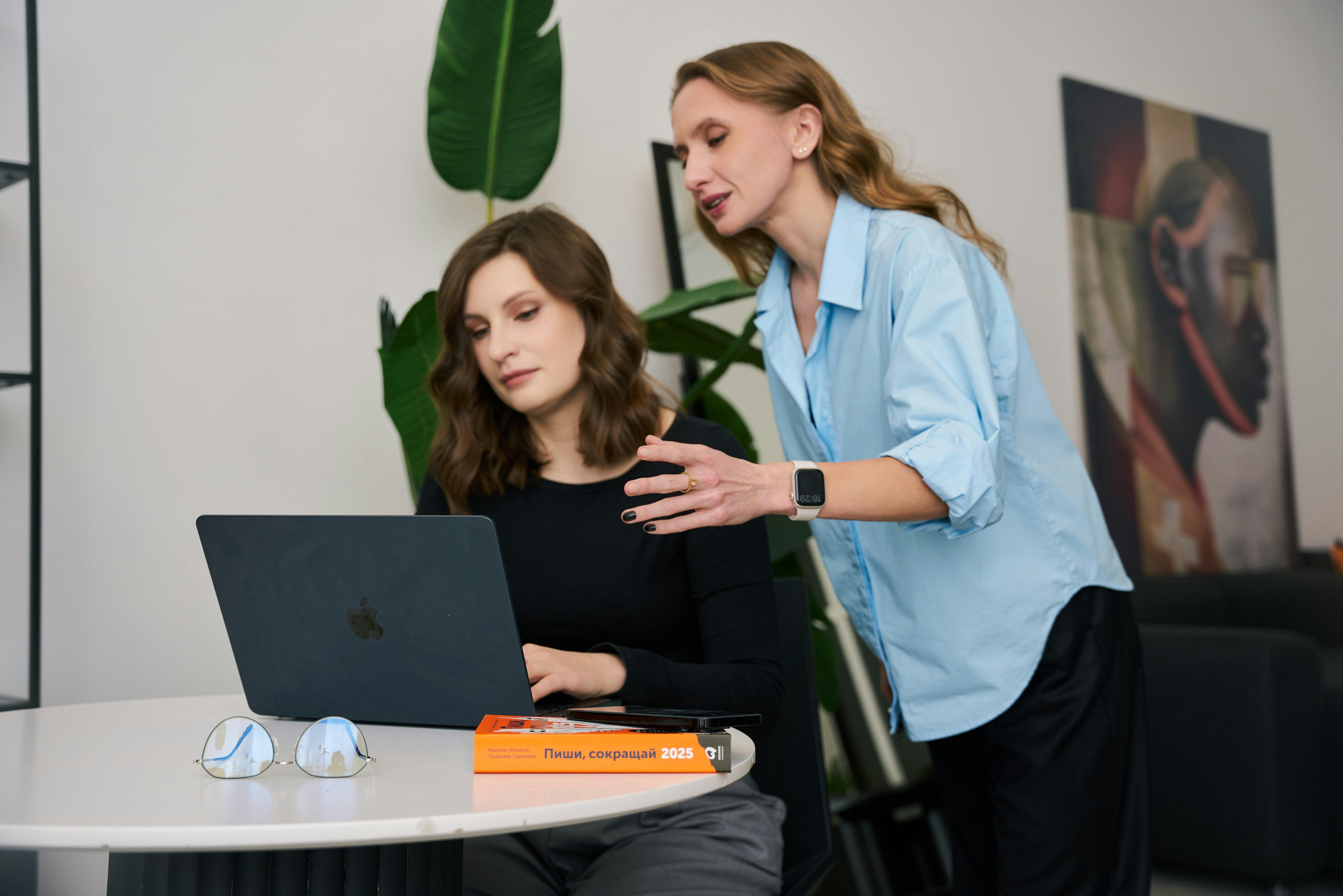 a woman standing next to a woman on a laptop