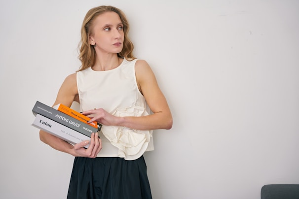 Portrait of a smiling female professor holding books with the college building softly blurred in the background.