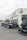 Two black sports cars are parked in front of a modern auto dealership with large glass windows and a sign displaying 'DRIVE AUTOMOBILES'. The overcast sky creates a neutral backdrop for the sleek vehicles.