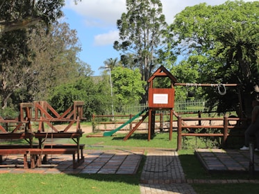 A serene outdoor play area featuring modern wooden structures surrounded by lush greenery.