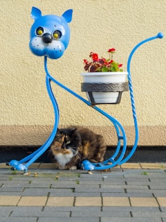 A whimsical crochet cat with soft yarn textures, posed beside a small potted plant.