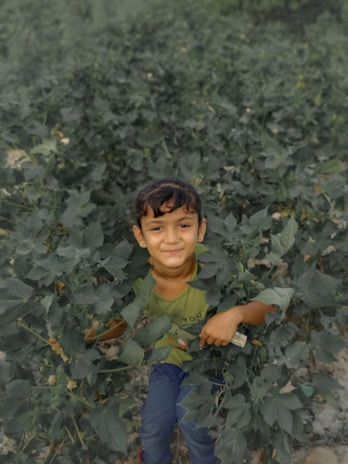 A childhood photo of a smiling child playing outdoors surrounded by nature.