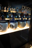 A serene museum-like display showcasing bottles of olive oil and tea with informational plaques in a softly lit room.