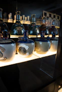 A serene museum-like display showcasing bottles of olive oil and tea with informational plaques in a softly lit room.